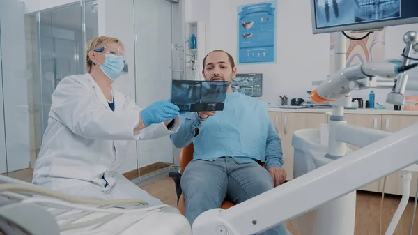 Стоматолог показывает результаты рентгена протеза пациенту во время осмотра — стоковое фото