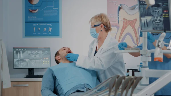 入れ歯を検査するために歯科用ツールを使用して顔マスクを持つ歯科医 — ストック写真