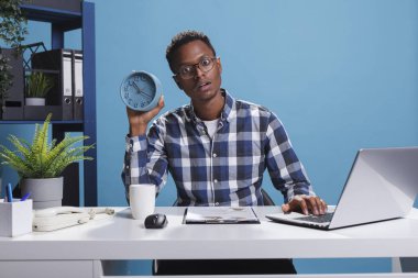 Şok ifadesine sahip şirket işadamı iş bilgisayarını kullanırken çalar saat takıyor.