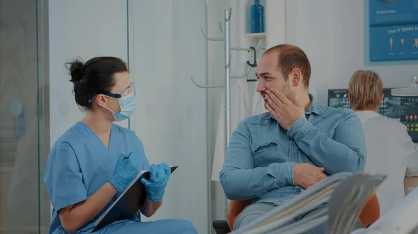 Пацієнт, який пояснює зубний біль стоматологічній медсестрі під час візиту до стоматології — стокове фото