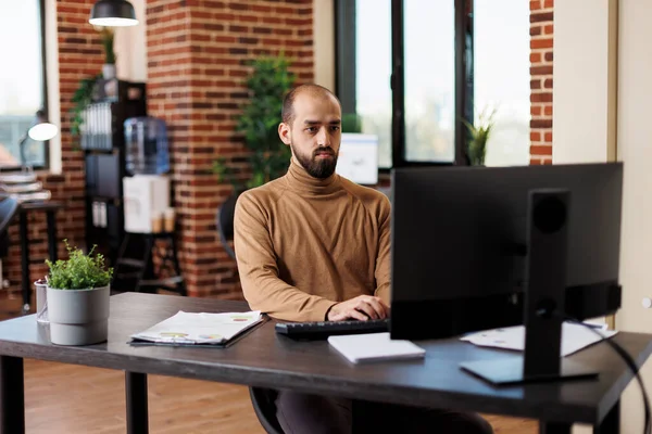 Joven director de proyecto que trabaja en las cartas financieras mientras está sentado en el escritorio utilizando el ordenador de trabajo. — Foto de Stock