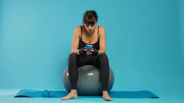 Atleta prendendo pausa per utilizzare smartphone e rilassarsi sulla palla tonificante — Foto Stock