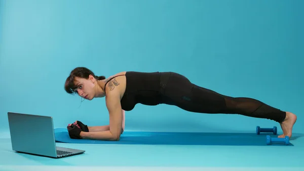 Athete sitting in plank position on yoga mat over blue background