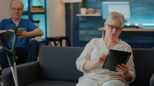 Oude vrouw met digitale tablet met touchscreen in de woonkamer — Stockfoto