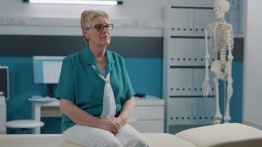 Sağlık muayenehanesinde oturan yaşlı kadının portresi.