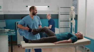Osteopati kabinesinde kasları açmak için bacakları kaldıran yaşlı bir insan.