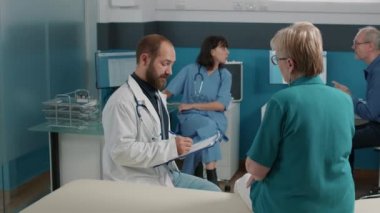 Erkek doktor not alıyor ve yaşlı insana danışıyor.