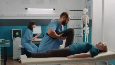 Bacak egzersizi yapan hekim yaşlı hastaya bacak açmak için egzersiz yapıyor.