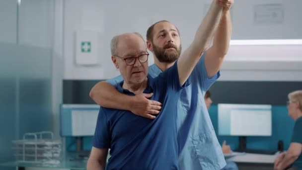 Yaşlı birinin kollarını kaldırarak kaslarını esneten tıbbi asistan. — Stok video