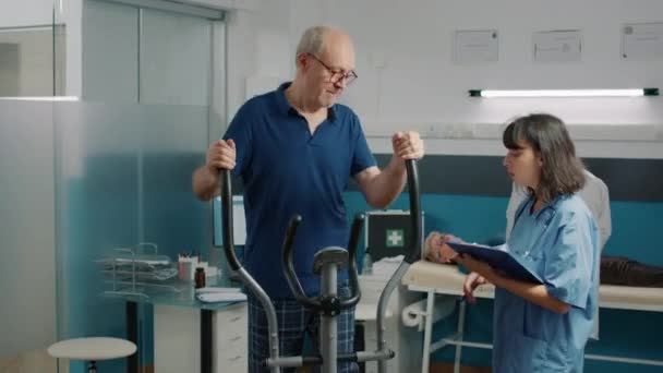 Paciente mayor haciendo ejercicio de recuperación en bicicleta estacionaria — Vídeo de stock