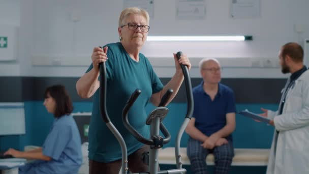 Portret van een oudere vrouw die lichaamsbeweging doet op een vaste fiets — Stockvideo