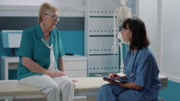 Женщина-медсестра делает заметки по файлам после обследования со старым пациентом — стоковое видео