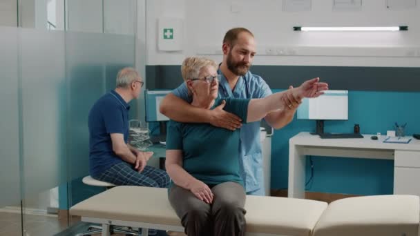 Orhopedyczny specjalista wykonujący ćwiczenia rozciągania ramion ze starszym pacjentem — Wideo stockowe