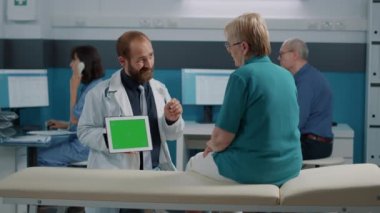 Doktor ve yaşlı kadın yatay yeşil ekrana bakıyor.