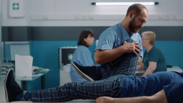 Male osteopath cracking legs bones and helping old man with muscles stretch — Stock Video