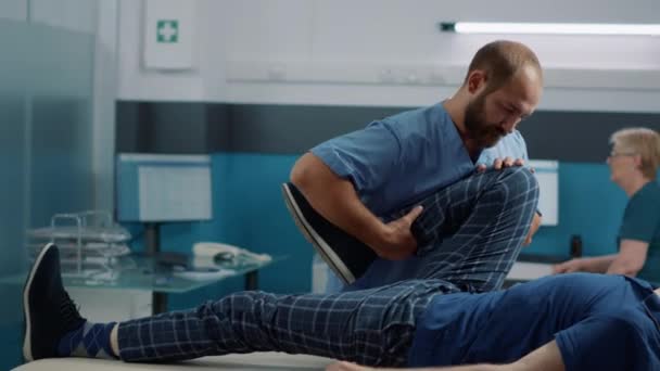 Специалист по остеопатии растягивает мышцы ног пожилого пациента — стоковое видео