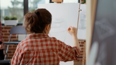 Vazo modeli çizmek için sanat atölyesine katılan genç bir kadın.