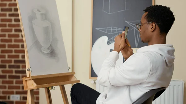 Африканський студент - американець, користуючись смартфоном, малює — стокове фото