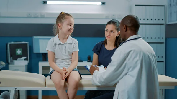 Маленькая девочка разговаривает с врачом на осмотре в кабинете — стоковое фото