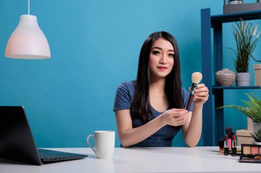 Elinde kozmetik fırçalar tutan gülümseyen içerik yaratıcısının portresi