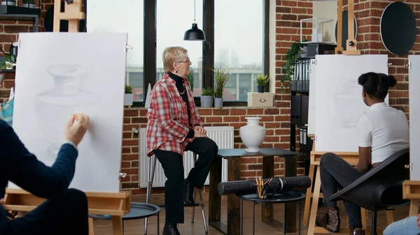 Mulher sênior explicando visão artística para as pessoas na aula de arte — Fotografia de Stock