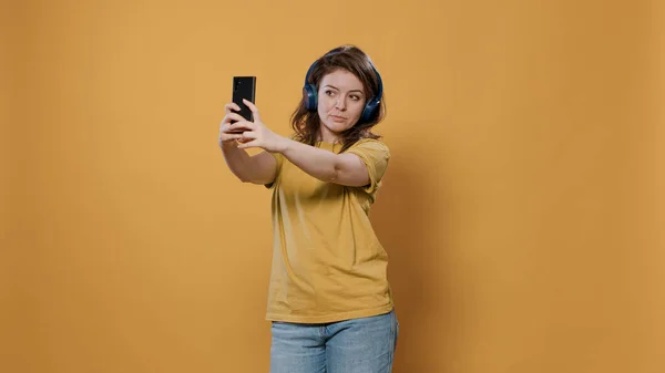 Mujer casual tomando una selfie usando un teléfono móvil mientras escucha música en auriculares inalámbricos — Foto de Stock