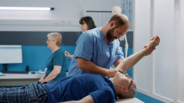 Fizyoterapist, yaşlı hastaya kol kaslarını esnetmesi için yardım ediyor.