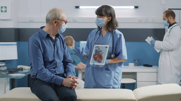 心臓病のイラストを見ている看護師と高齢者 — ストック写真