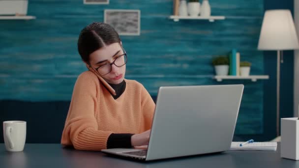 Junge Frau telefoniert und nutzt Laptop am heimischen Schreibtisch — Stockvideo