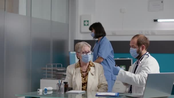 Mannelijke arts die otoscoop gebruikt om ooronderzoek te doen met gepensioneerde persoon — Stockvideo