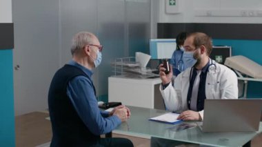 Erkek doktor yaşlı adama ilaç şişesiyle tıbbı anlatıyor.