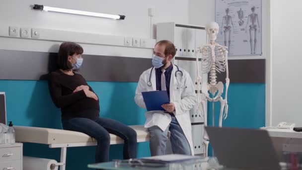 Lekarz robiący notatki na papierach podczas wizyty kontrolnej u pacjentki w ciąży — Wideo stockowe