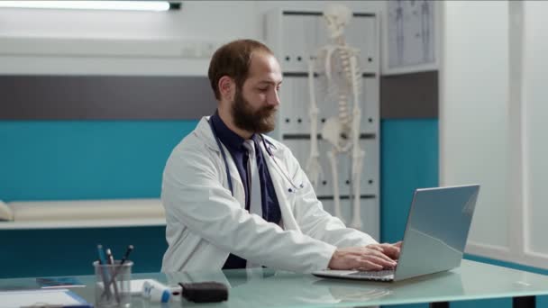 Retrato del médico general que trabaja en la computadora portátil para planificar la visita de chequeo — Vídeos de Stock
