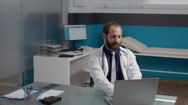 Retrato del médico general que trabaja en la computadora portátil en el consultorio médico — Vídeos de Stock
