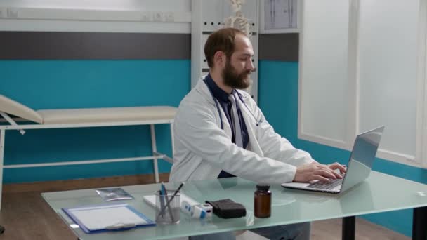Retrato de doctor masculino con uniforme usando el ordenador portátil en gabinete — Vídeos de Stock