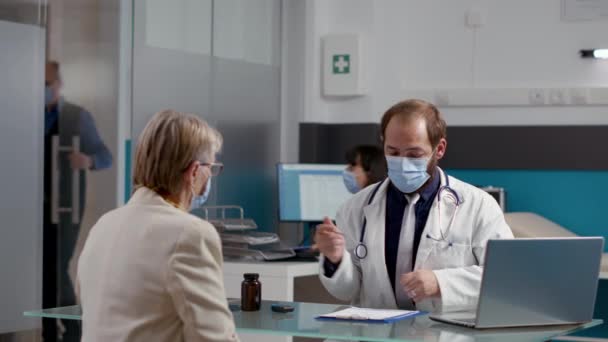 Mężczyzna lekarz robi notatki na receptę, aby pomóc pacjentowi — Wideo stockowe