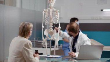 Doktor osteopati teşhisini açıklamak için insan iskeletini işaret ediyor.