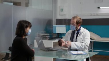 Erkek doktor yüz maskesi takan hasta hastaya bir şişe hap veriyor.