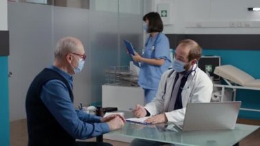 Erkek doktor, ihtiyarla olan randevusuna not alıyor.