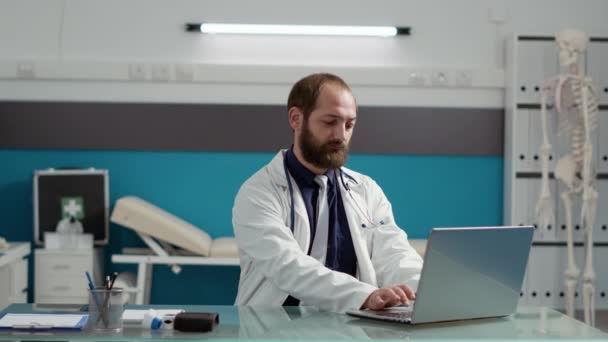 Retrato de un médico varón que usa un abrigo blanco y un portátil — Vídeos de Stock