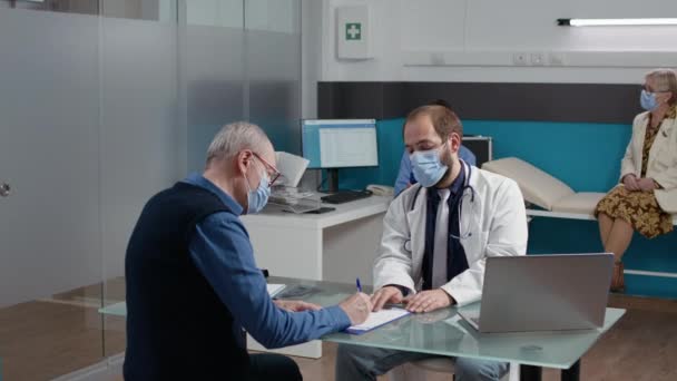 Senior Patient unterschreibt Checkup-Papiere beim Arzttermin — Stockvideo