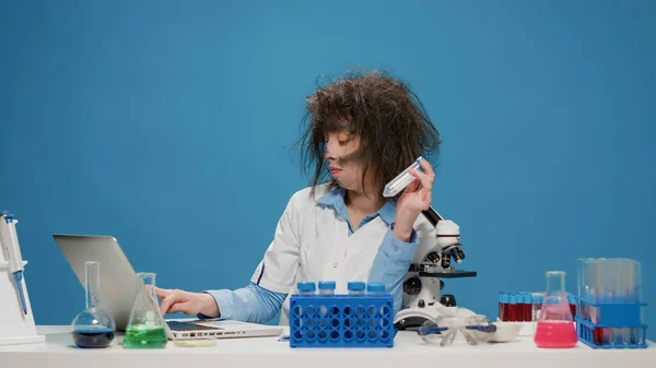 Забавна божевільна жінка-вчений дивиться на пробірки на столі — стокове фото