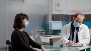 Doktor not alıyor ve kadın hastaya reçeteli kağıt veriyor.