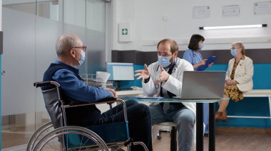 Doktor tekerlekli sandalyedeki hastaya muayene yapıyor.