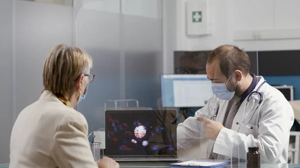 Health specialist showing virus illustration on laptop to old woman — Stock Photo, Image