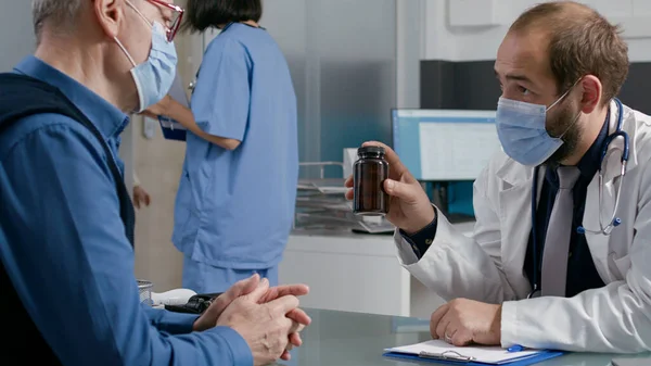 男性医師が老人に薬のボトルで薬を説明する — ストック写真