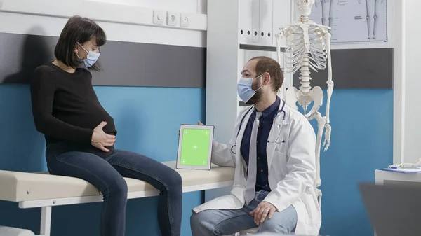 Hamile kadın ve doktor dijital tablette yeşil ekrana bakıyor — Stok fotoğraf