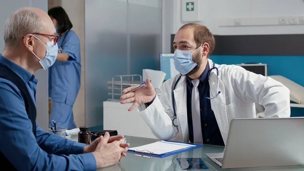 Male doctor taking notes at consultation appointment with old man — Stock Photo, Image