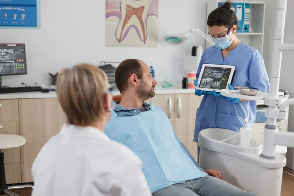 Медсестра-стоматолог держит планшетный компьютер, объясняя экспертизу рентгенографии — стоковое фото