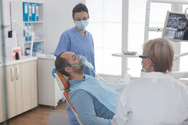 Женщина-медсестра смотрит на пациента в кислородной маске обсуждая лечение кариеса — стоковое фото